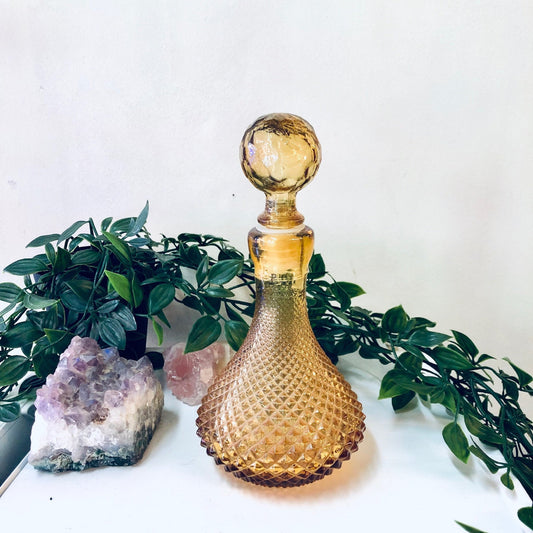 Vintage yellow glass lidded decanter perfume bottle with rubber stopper, made in Italy, displayed with amethyst geode and greenery for home decor.