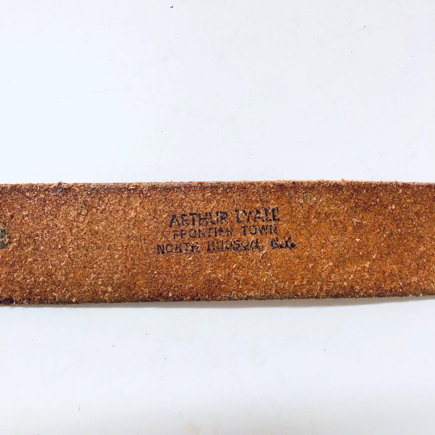 Vintage brown leather cowboy belt with "ARTHUR LYAM FEED STORE NORTH PLATTE, NEB." engraved on the back, small skinny size with hook buckle closure in a southwestern style.