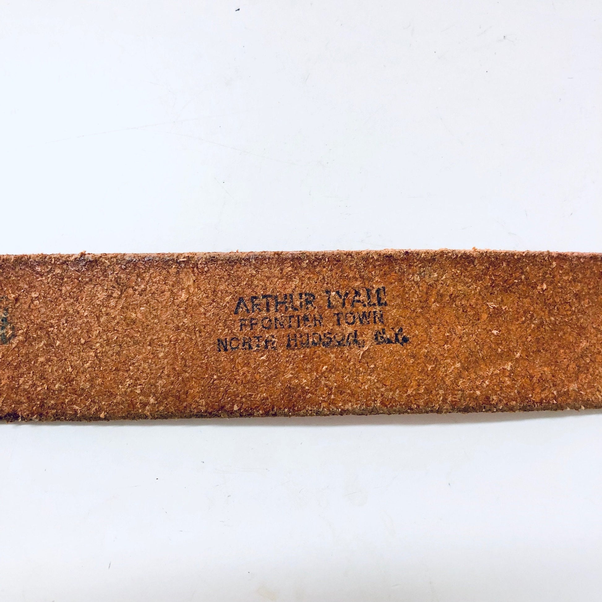 Vintage brown leather cowboy belt with "ARTHUR LYAM FEED STORE NORTH PLATTE, NEB." engraved on the back, small skinny size with hook buckle closure in a southwestern style.