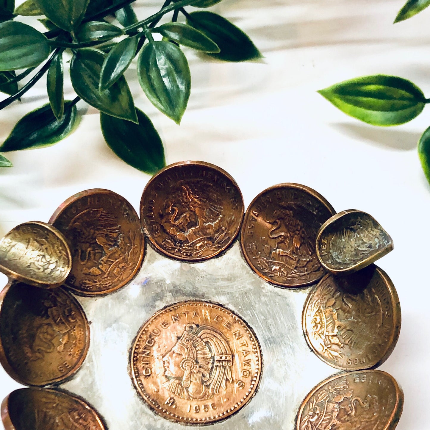 Vintage Mexican coin ashtray made of copper centavos, surrounded by green leaves, used as a decorative catch-all dish, ring tray or display piece for foreign currency coins.