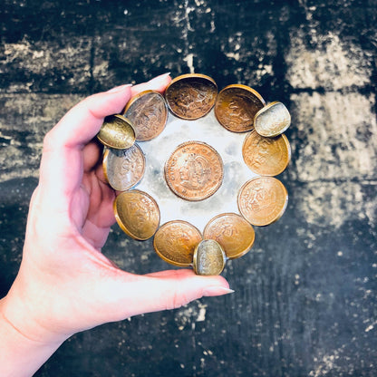 Vintage copper Mexican coin ashtray used as a catch-all dish, ring tray, or decorative coin display on a textured background, held in a person's hand.