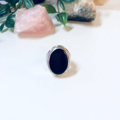 Vintage silver ring with oval-shaped black onyx stone on white background with rose quartz and plant leaves