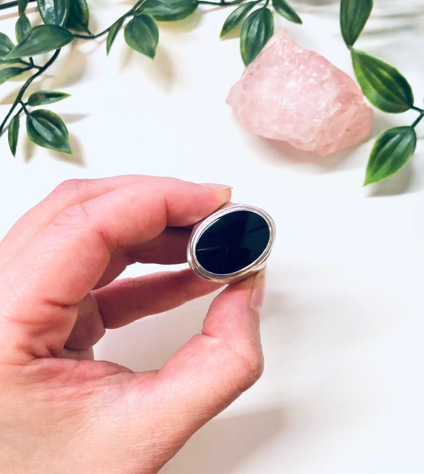 Vintage silver ring with oval black onyx stone, held in front of rose quartz and greenery