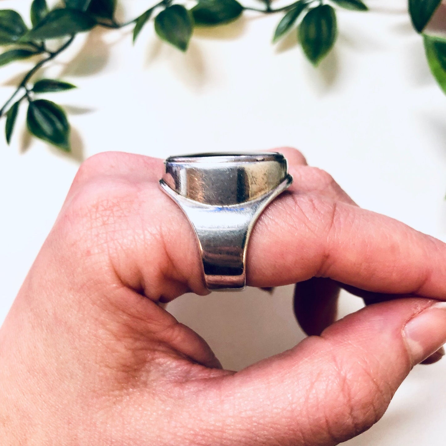 Vintage silver ring with black oval onyx stone held between hands in front of leafy background