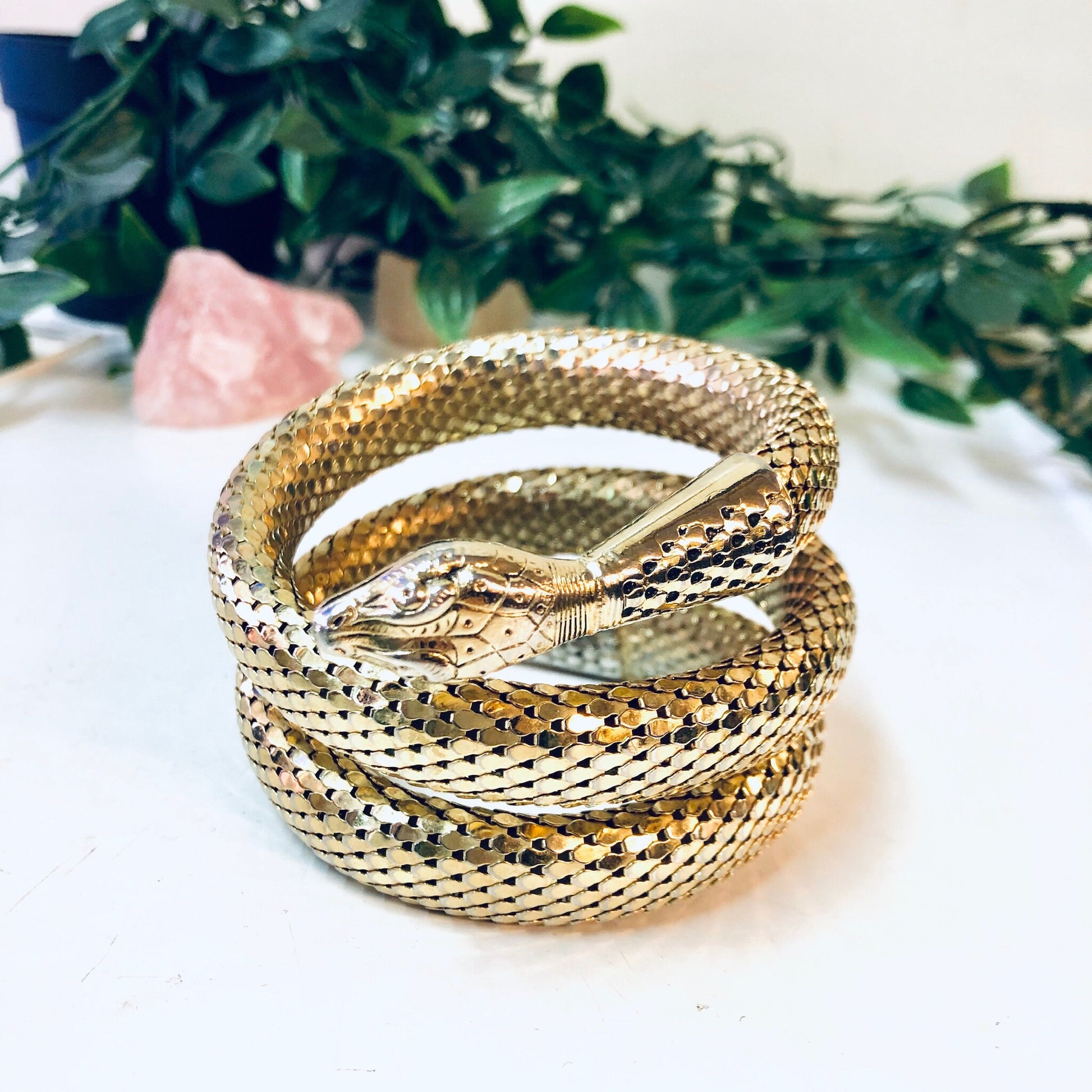 Vintage gold-toned Whiting and Davis mesh snake bracelet coiled on white surface with green foliage in background