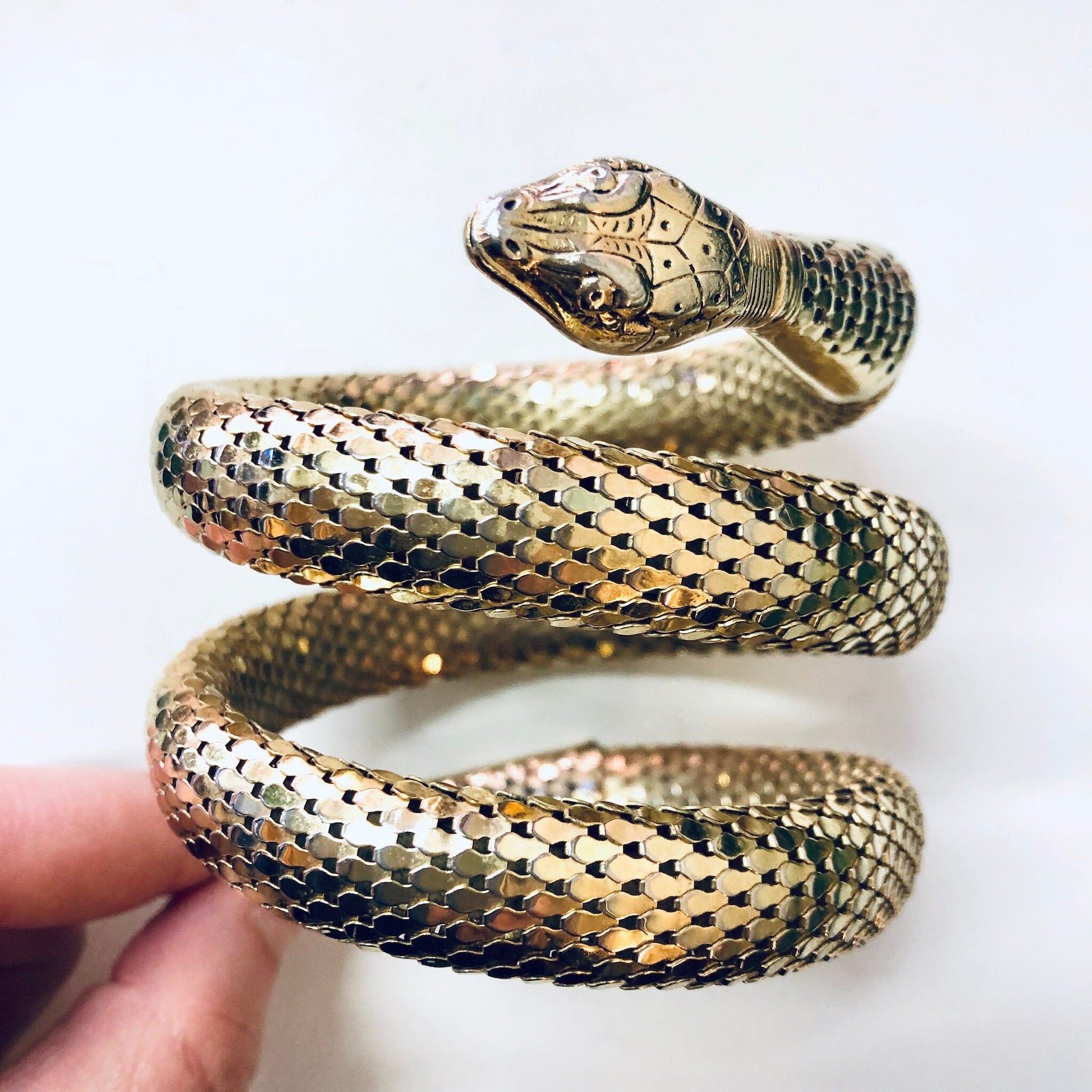 Vintage gold-toned Whiting and Davis mesh snake bracelet coiled around itself, resembling a real snake, held in a person's hand against a white background.