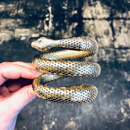 Golden coiled snake mesh bracelet made by Whiting and Davis held in hand against grunge textured background