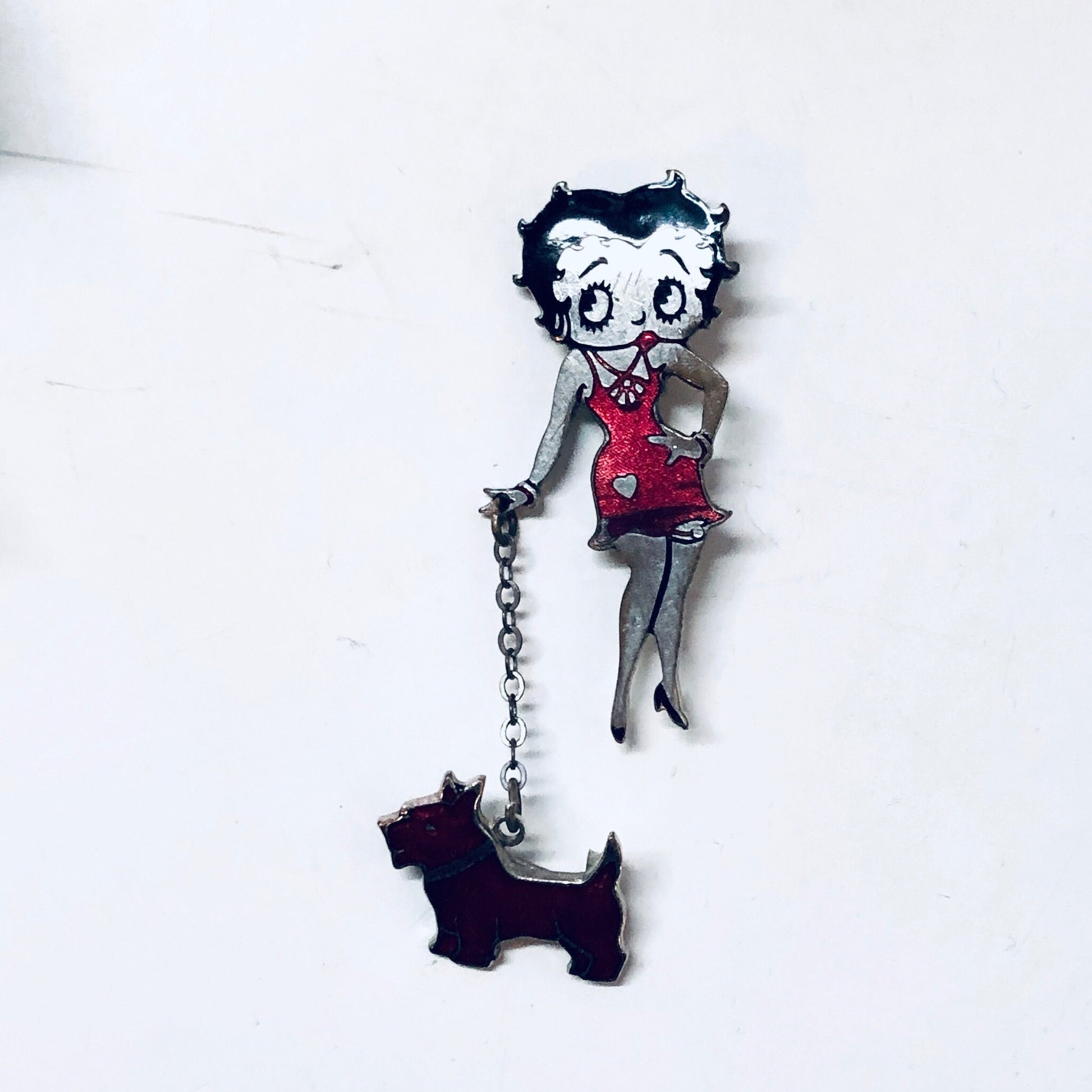 Betty Boop vintage silver-tone pin featuring the iconic cartoon character in her signature flapper girl outfit with a red dress and black hair, accompanied by a small black dog charm dangling from a chain.