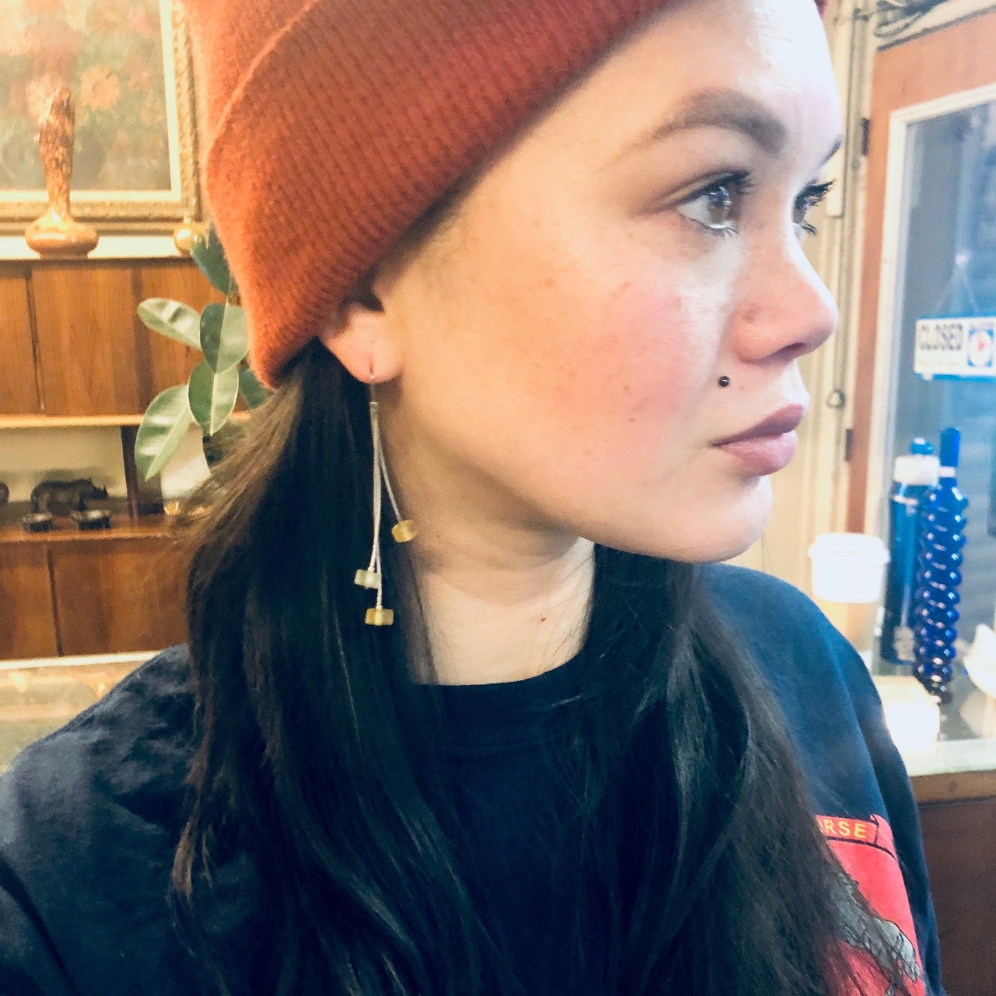 Close-up portrait of a young woman wearing a red knit beanie, black shirt, and statement earrings while looking off to the side with a pensive expression.