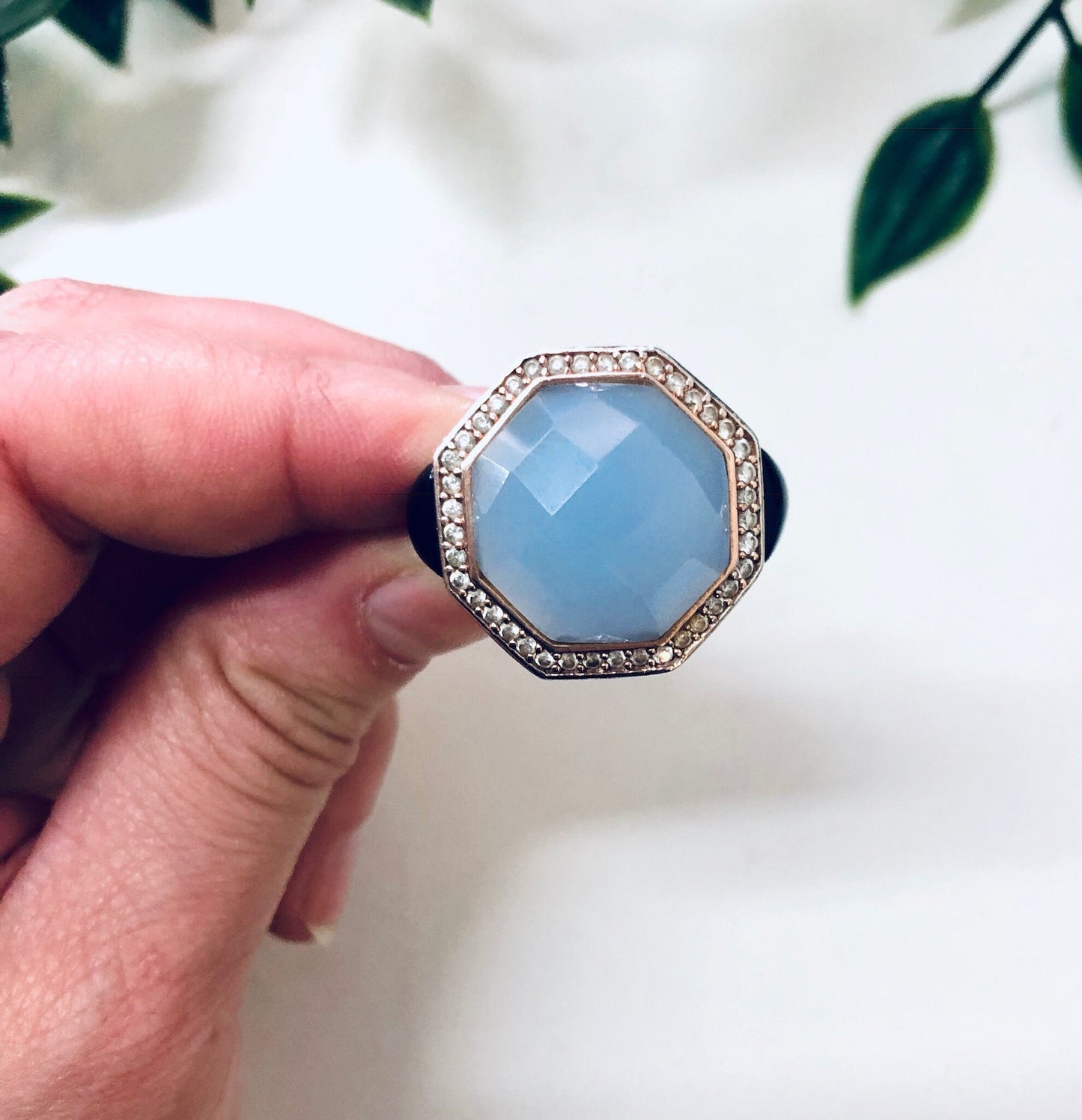 Vintage sterling silver cocktail ring with light blue faceted stone and intricate filigree design, held in hand against white floral background