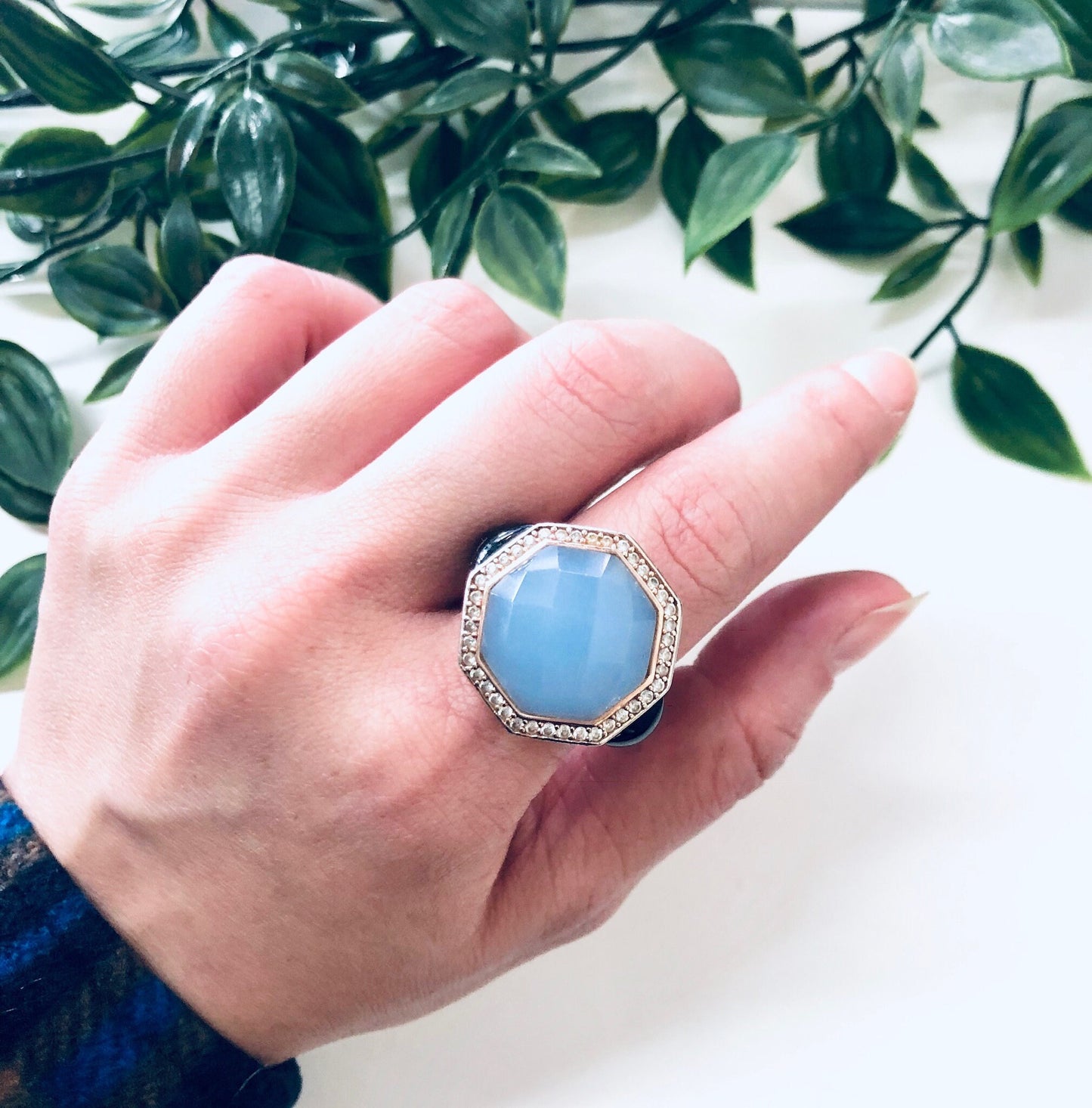 Vintage sterling silver cocktail ring with light blue stone and filigree detailing, held in front of green foliage background