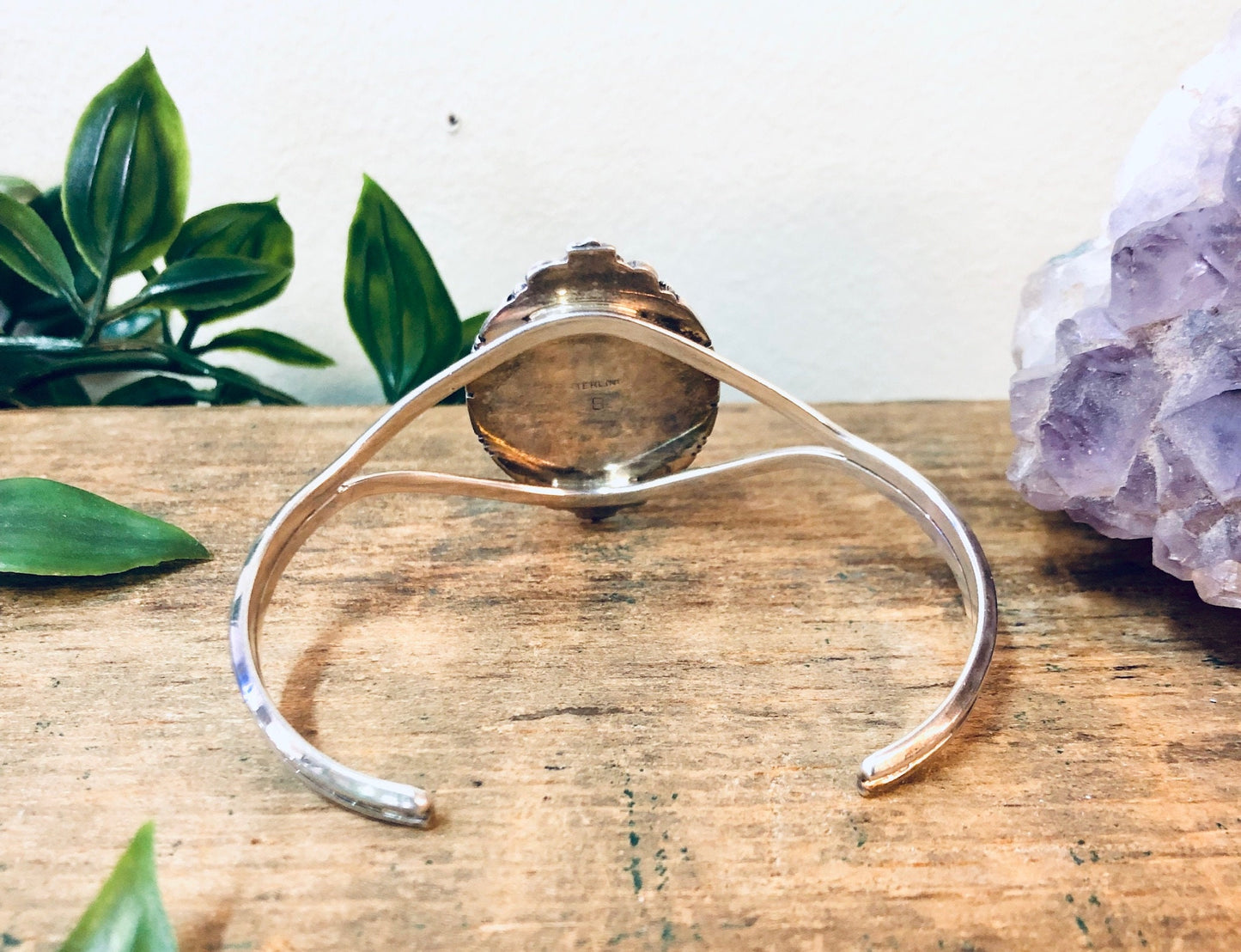 Vintage amber and silver cuff bracelet on wooden surface with amethyst crystal and green leaves