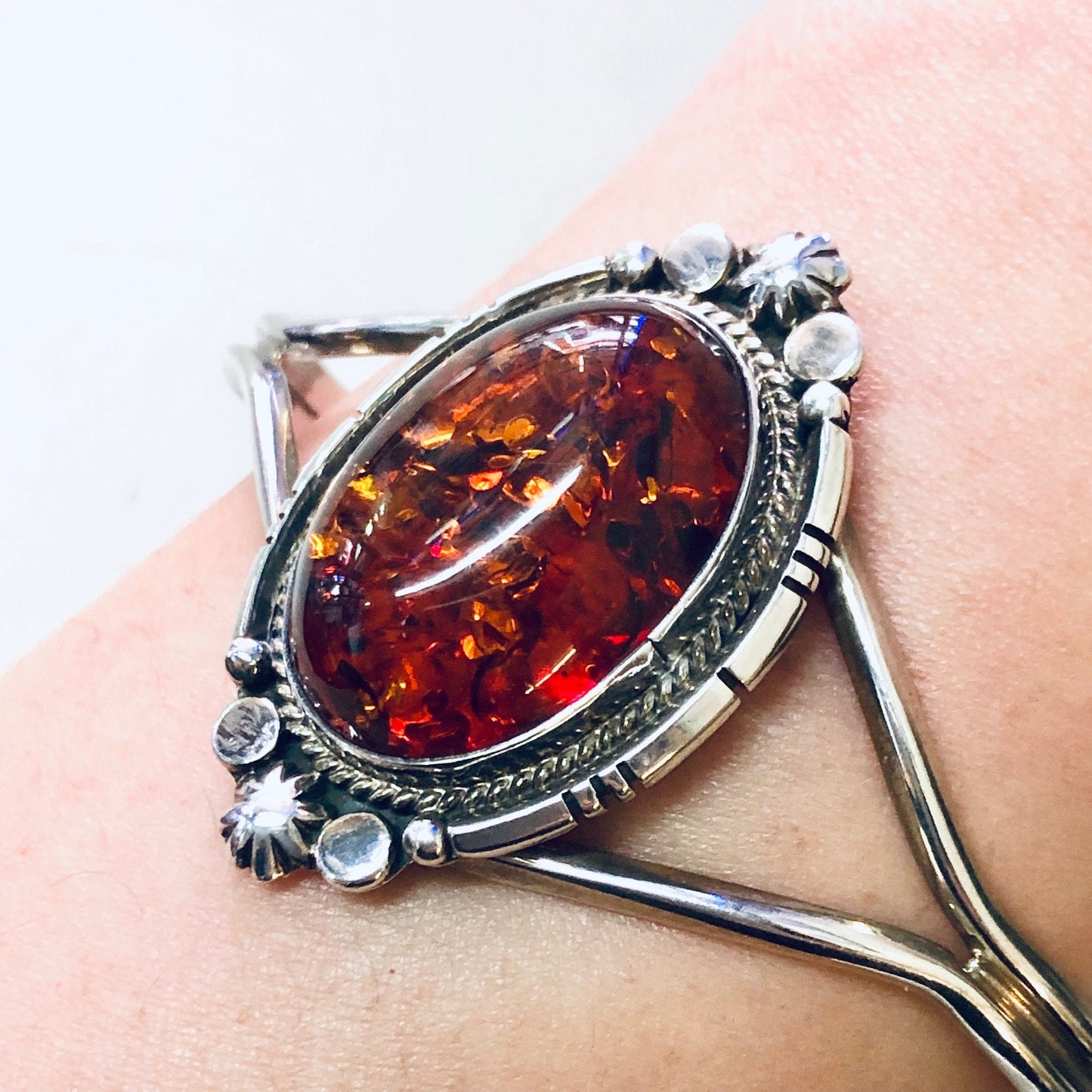 Vintage silver cuff bracelet with large oval amber gemstone, accented by clear crystals, displayed on peach fabric background.