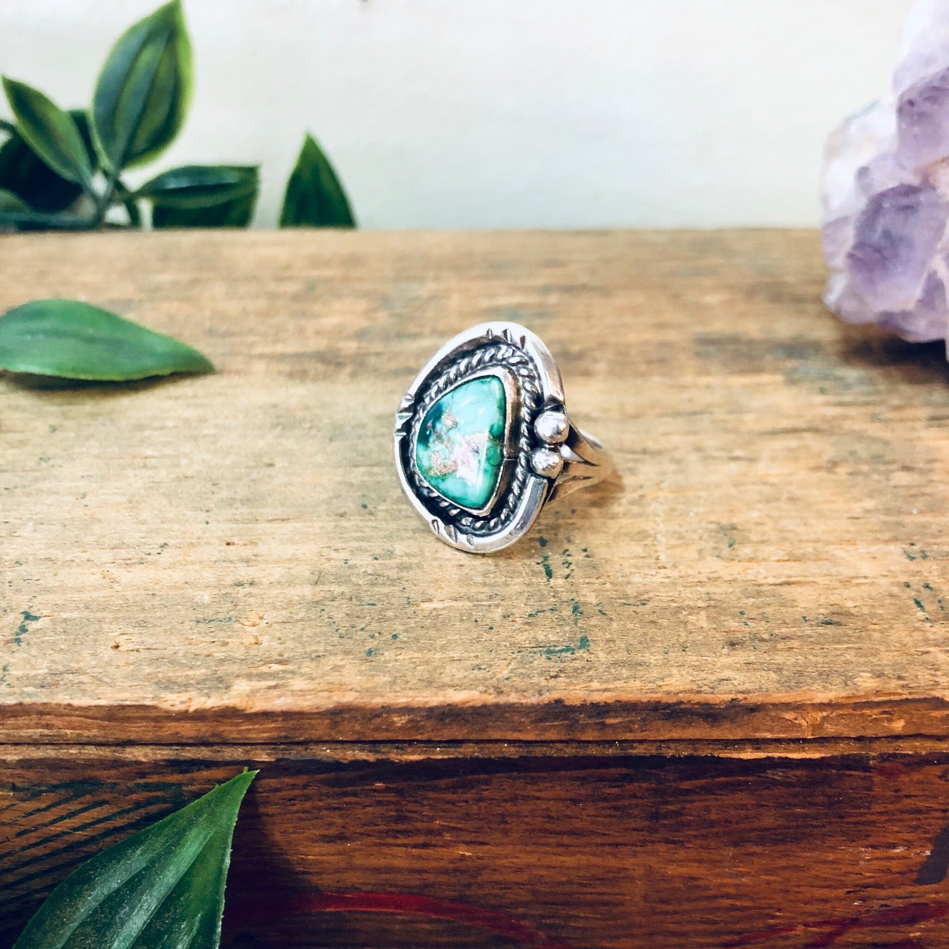 Vintage silver ring with green turquoise stone on rustic wooden surface surrounded by leaves and amethyst crystal