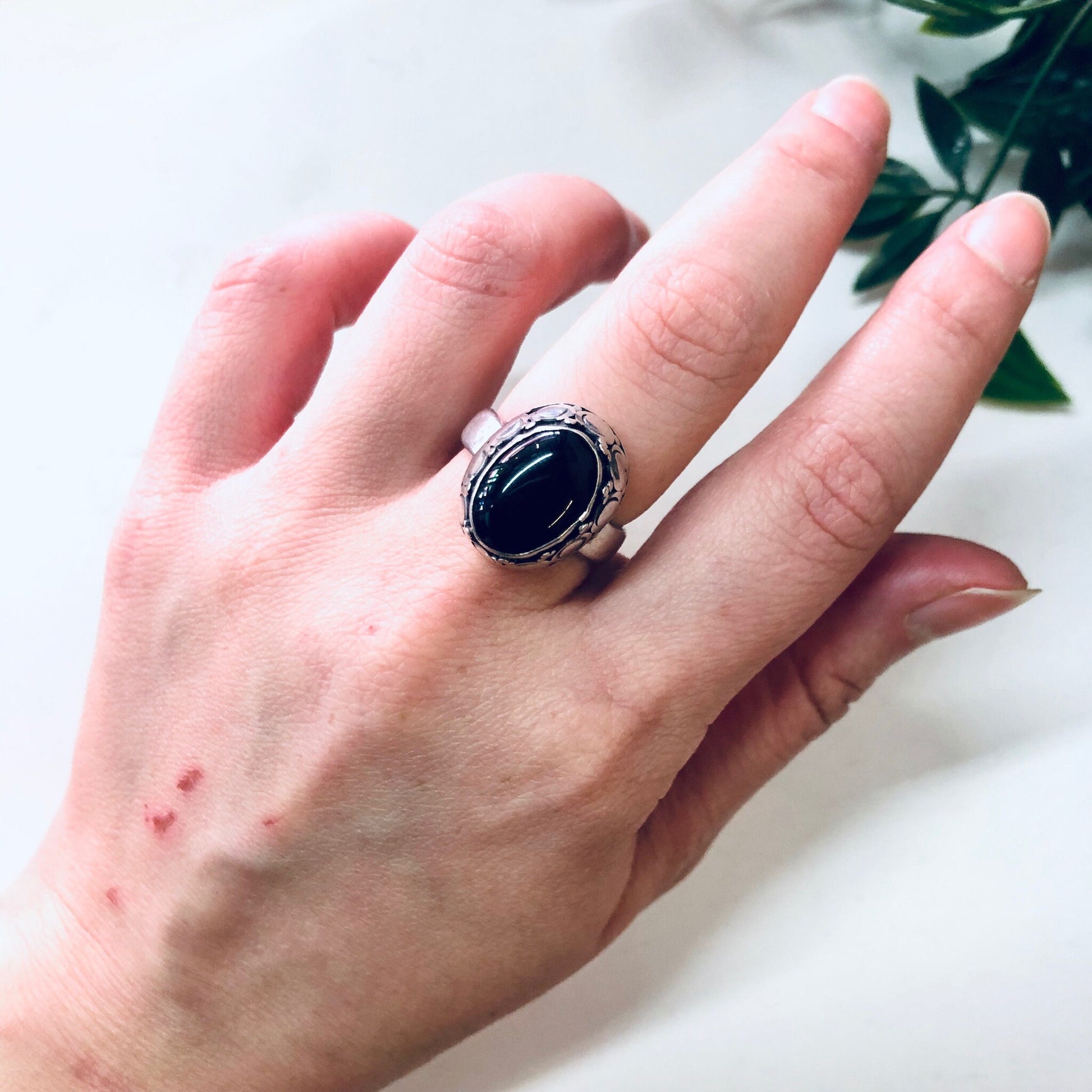 Vintage silver ring with oval black onyx gemstone on a hand next to greenery