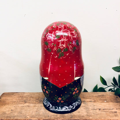 Hand-painted vintage Russian nesting doll set featuring intricate floral designs on a vibrant red and navy blue color scheme, signed by the artist and displayed on a wooden surface.