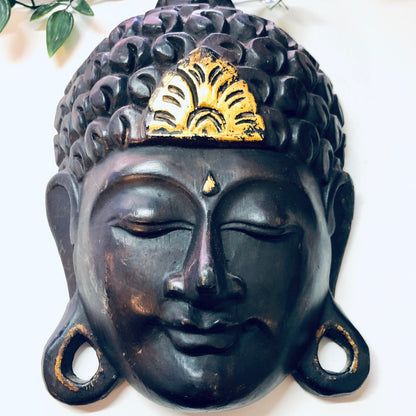Vintage wood carved mask with dark brown finish and gold accents, featuring serene Buddha face, for unique wall decor or Asian art display in home.