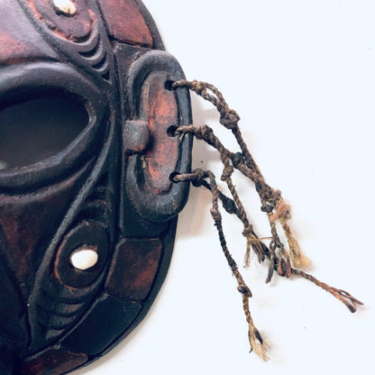 Antique carved wooden tribal mask with intricate details and braided rope hanging against a white background, a unique vintage home decor wall art piece