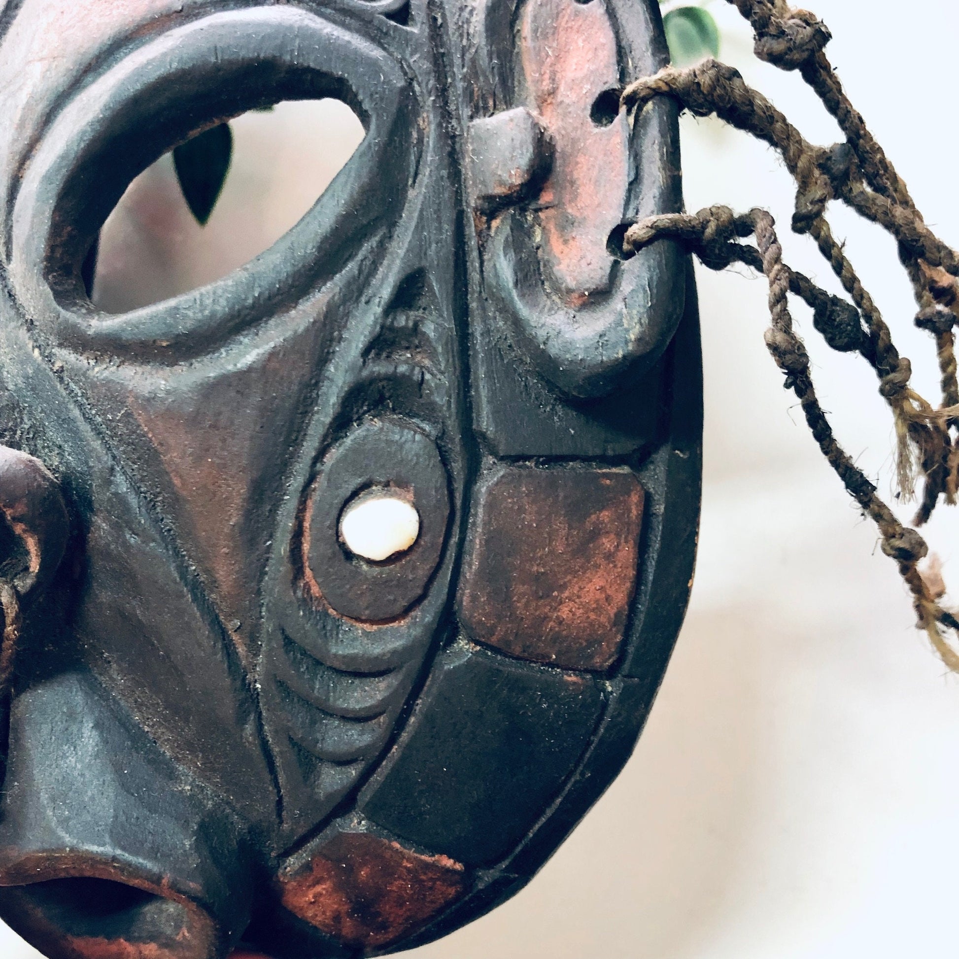 Alt text: Close-up view of a vintage hand-carved wooden mask with intricate detailing, cutout holes, and tribal-inspired design, hanging on a wall as unique home decor or wall art.