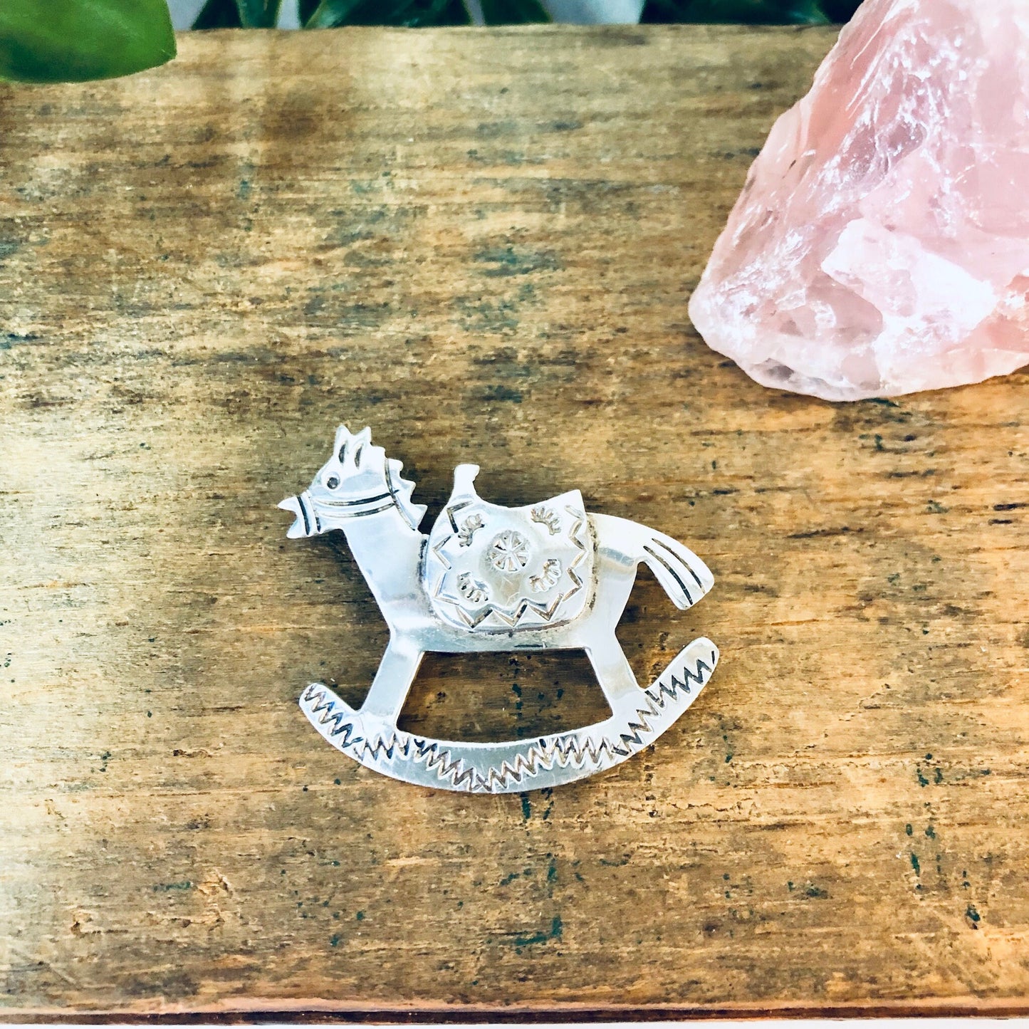 Vintage silver rocking horse brooch pin, made in Mexico, on rustic wooden surface with pink crystal.