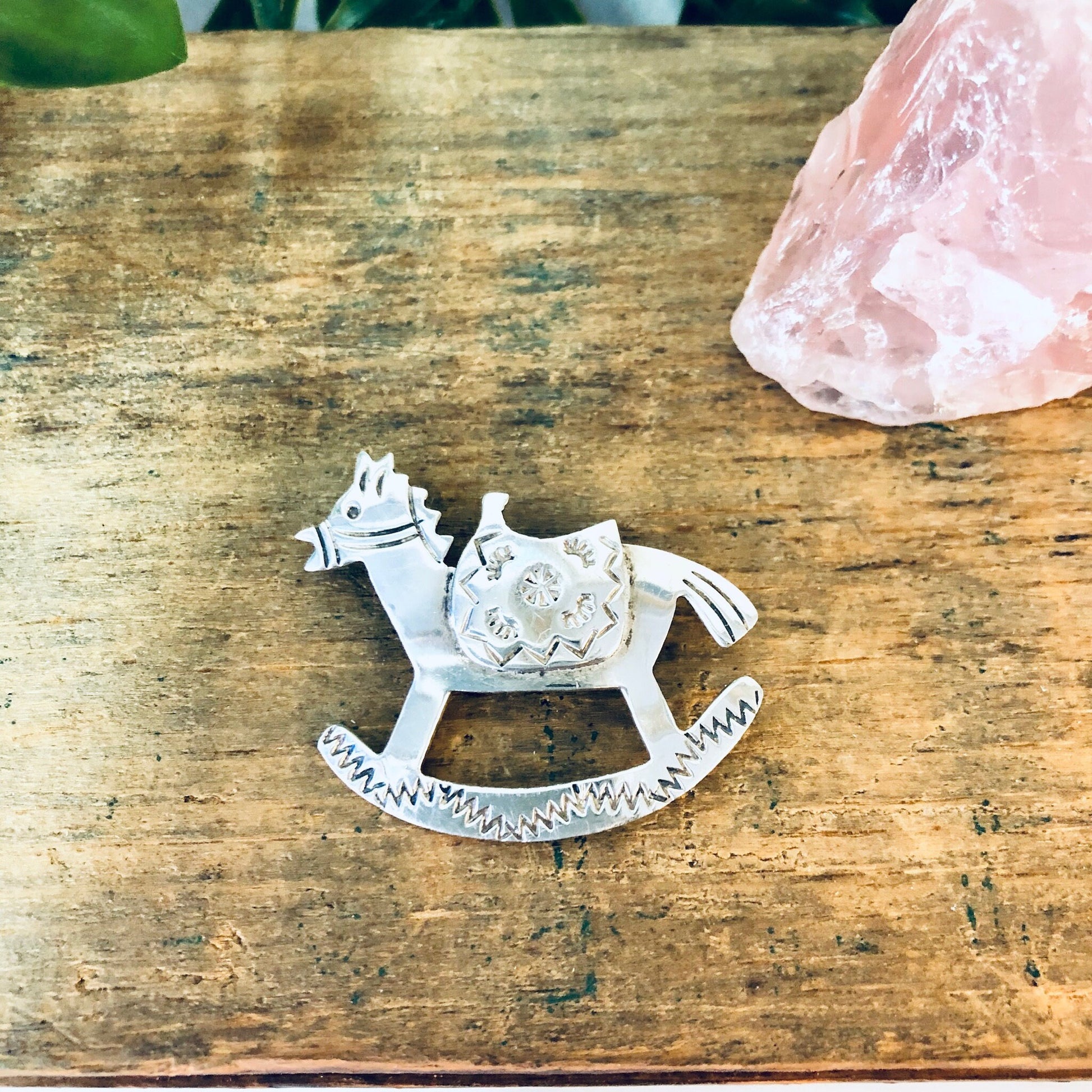 Vintage silver rocking horse brooch pin, made in Mexico, on rustic wooden surface with pink crystal.