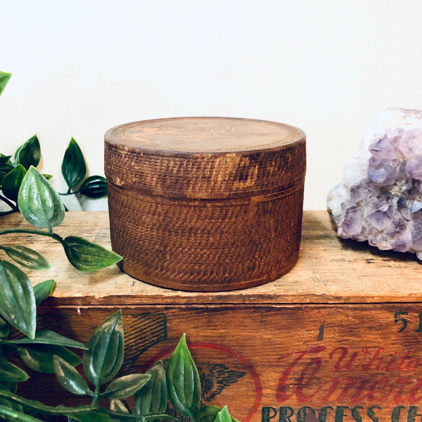 Round wooden carved trinket box on rustic table with plants and amethyst crystal