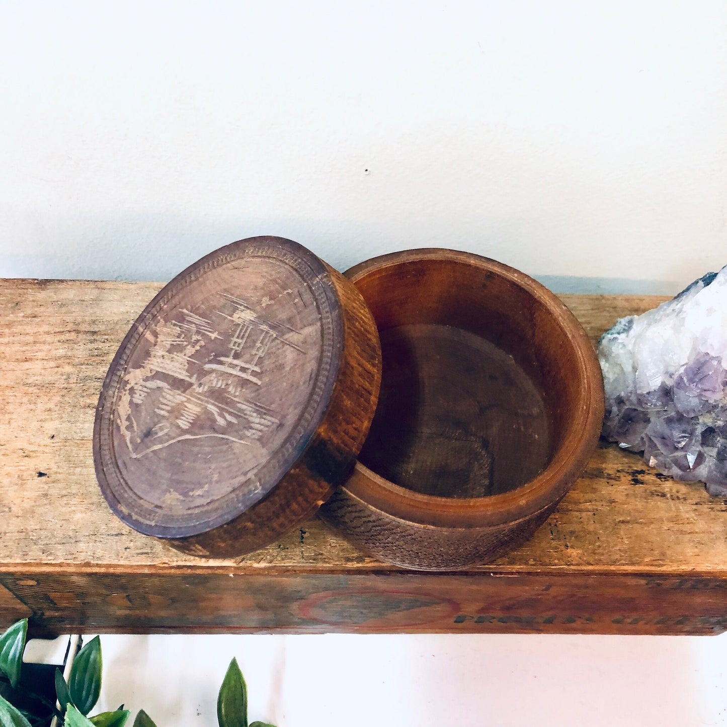 Vintage carved wooden jewelry box with rounded lid partially open, sitting on rustic wooden shelf with amethyst crystal cluster nearby