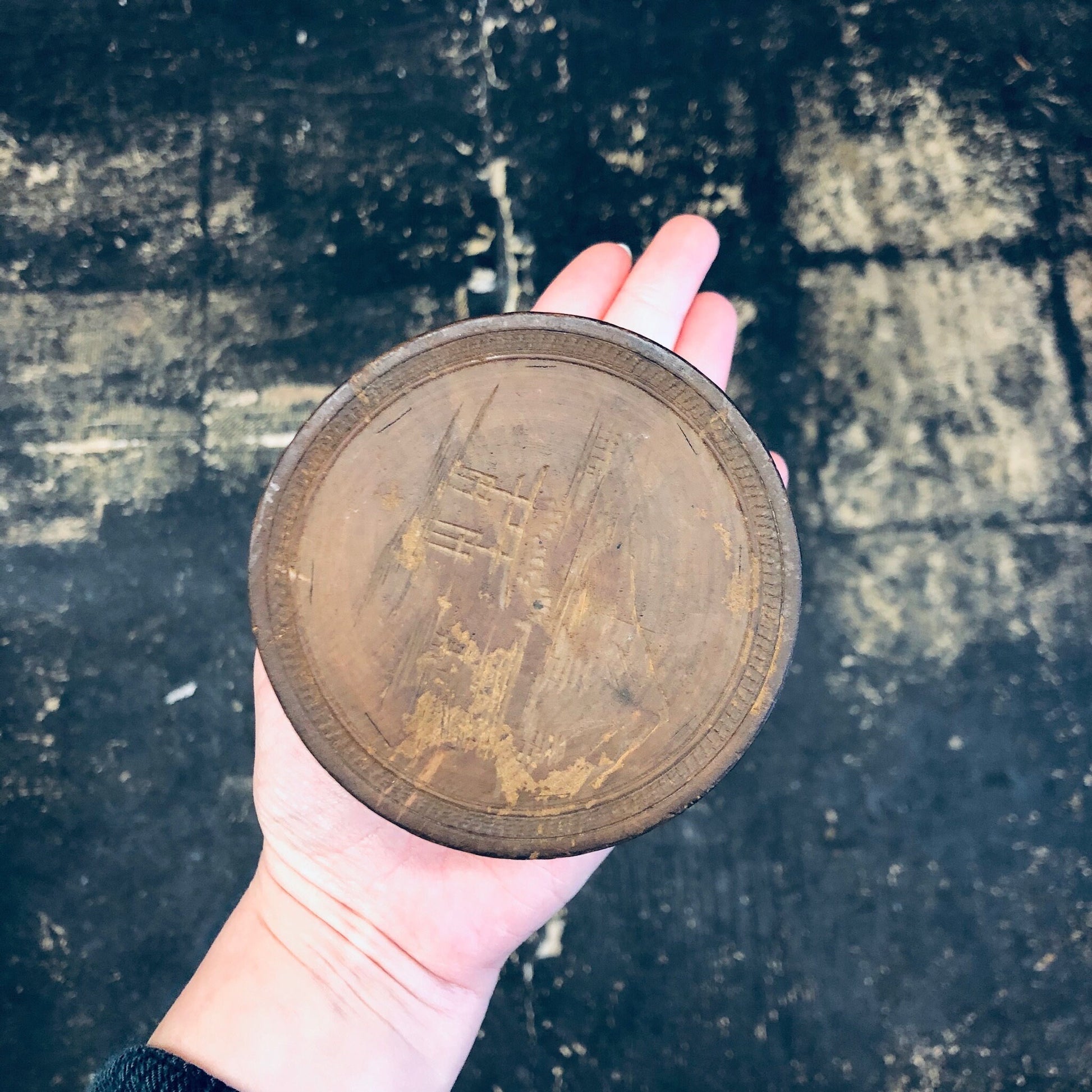 Hand holding a vintage round wooden trinket box with weathered rustic surface texture against a stone background
