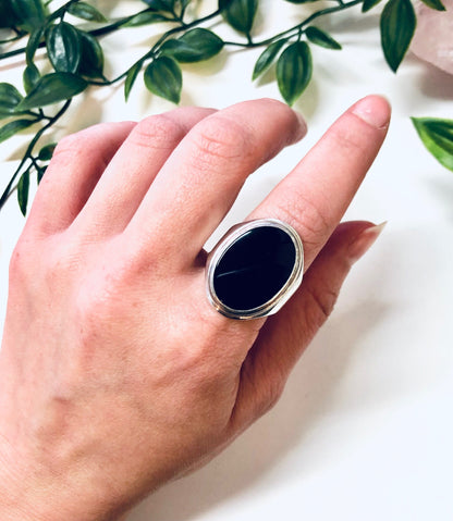 Vintage oval black onyx silver ring on hand next to green leaves