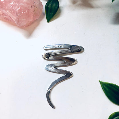 Vintage sterling silver abstract squiggle brooch pin jewelry, unique line design suitable for Valentine's Day gift, displayed with pink rose petals and green leaves.