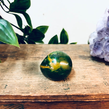 Green and yellow marbled plastic ring on weathered wooden surface with crystal and plant in background