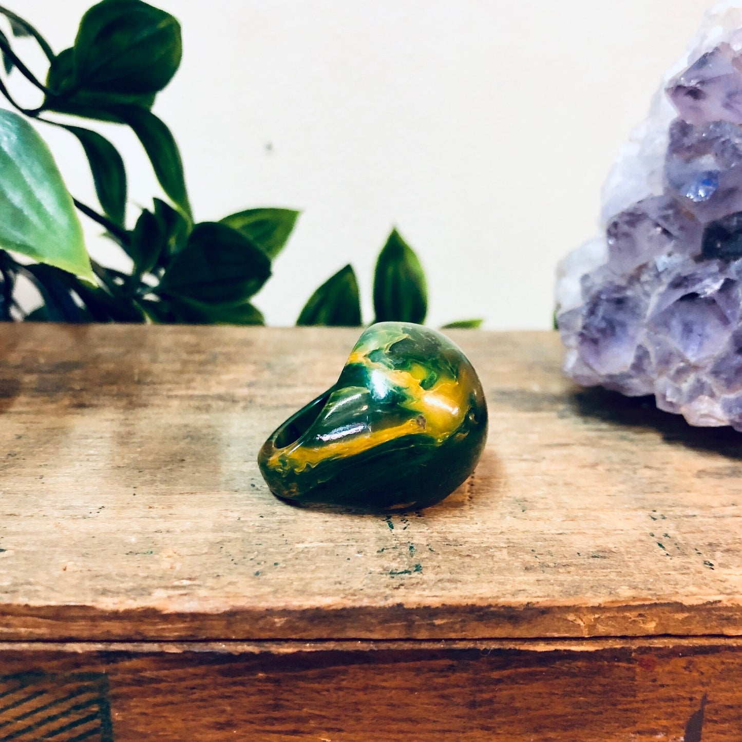 Green and yellow marbled plastic ring on wooden surface with amethyst crystal and plant in background, vintage retro statement jewelry gift idea for Valentine's Day