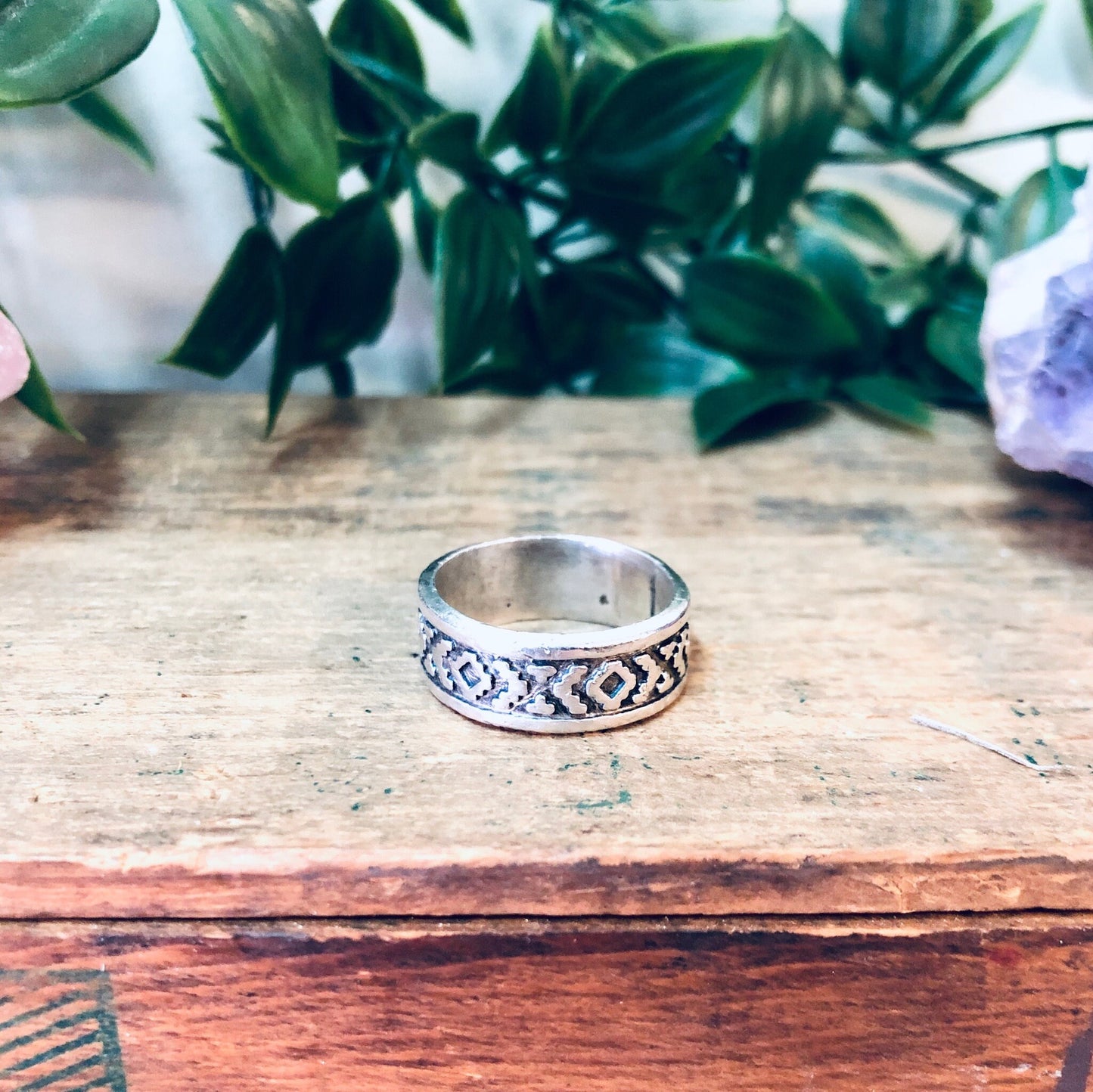 Vintage silver band ring with unique geometric design, displayed on rustic wooden surface with floral greenery in background, perfect as simple bohemian jewelry gift for mom or everyday wear.