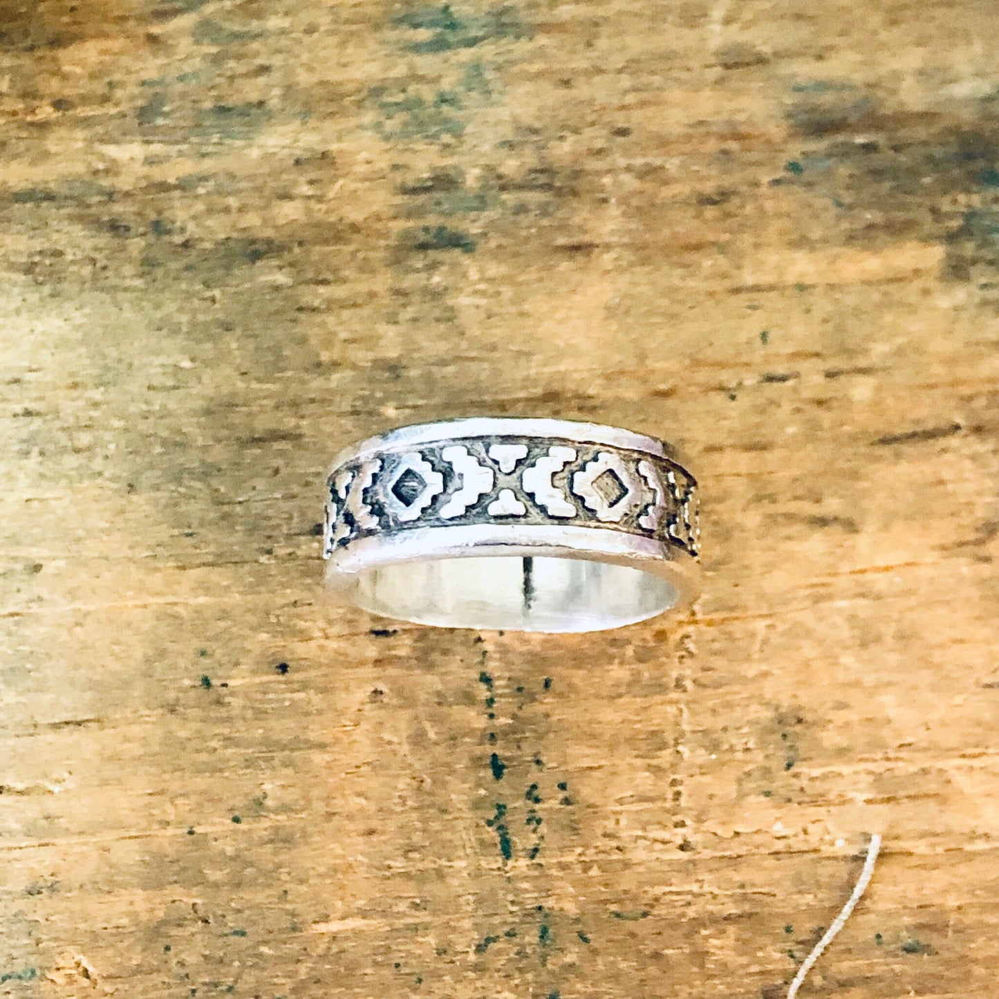 Vintage silver band ring with unique geometric design on weathered wooden surface