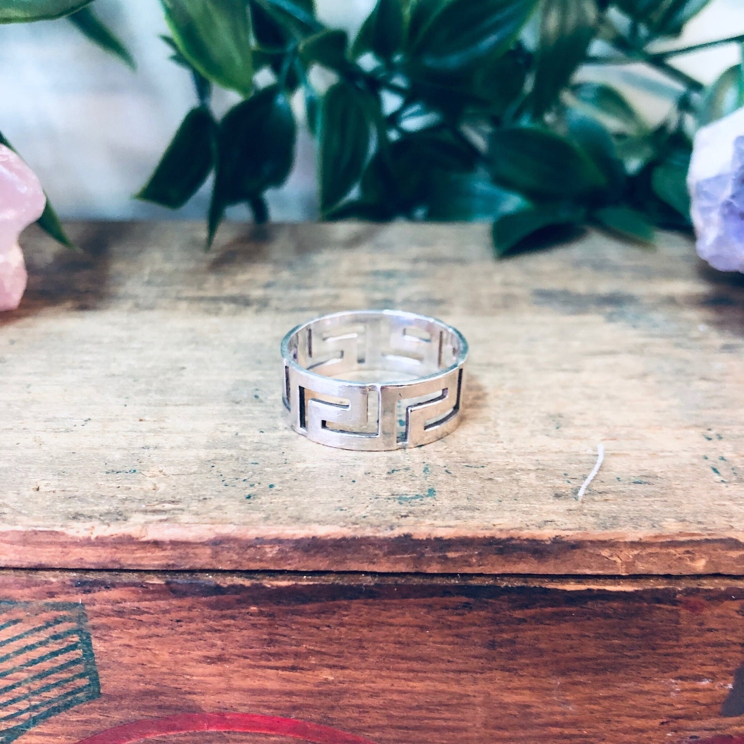 Vintage sterling silver cutout band ring on rustic wooden surface with flowers in background