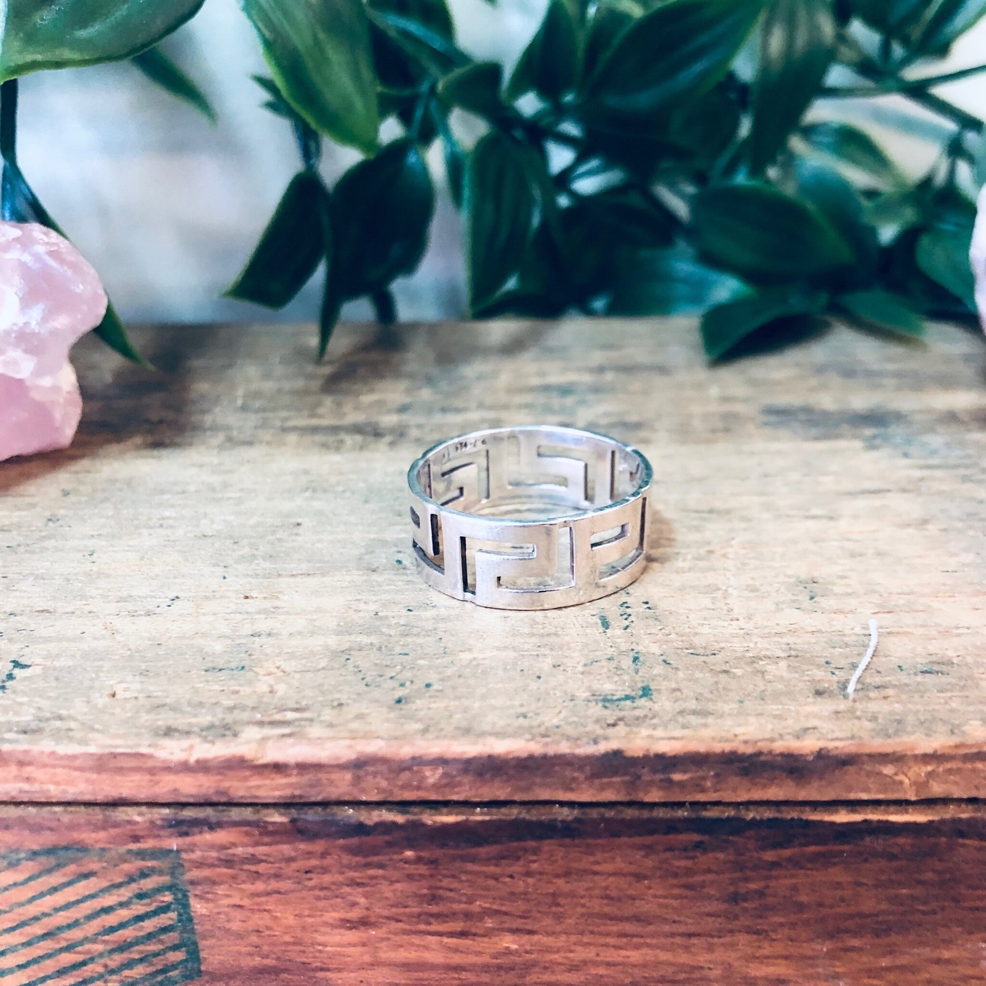 Vintage sterling silver cut-out band ring on wooden surface with plants and crystal in background