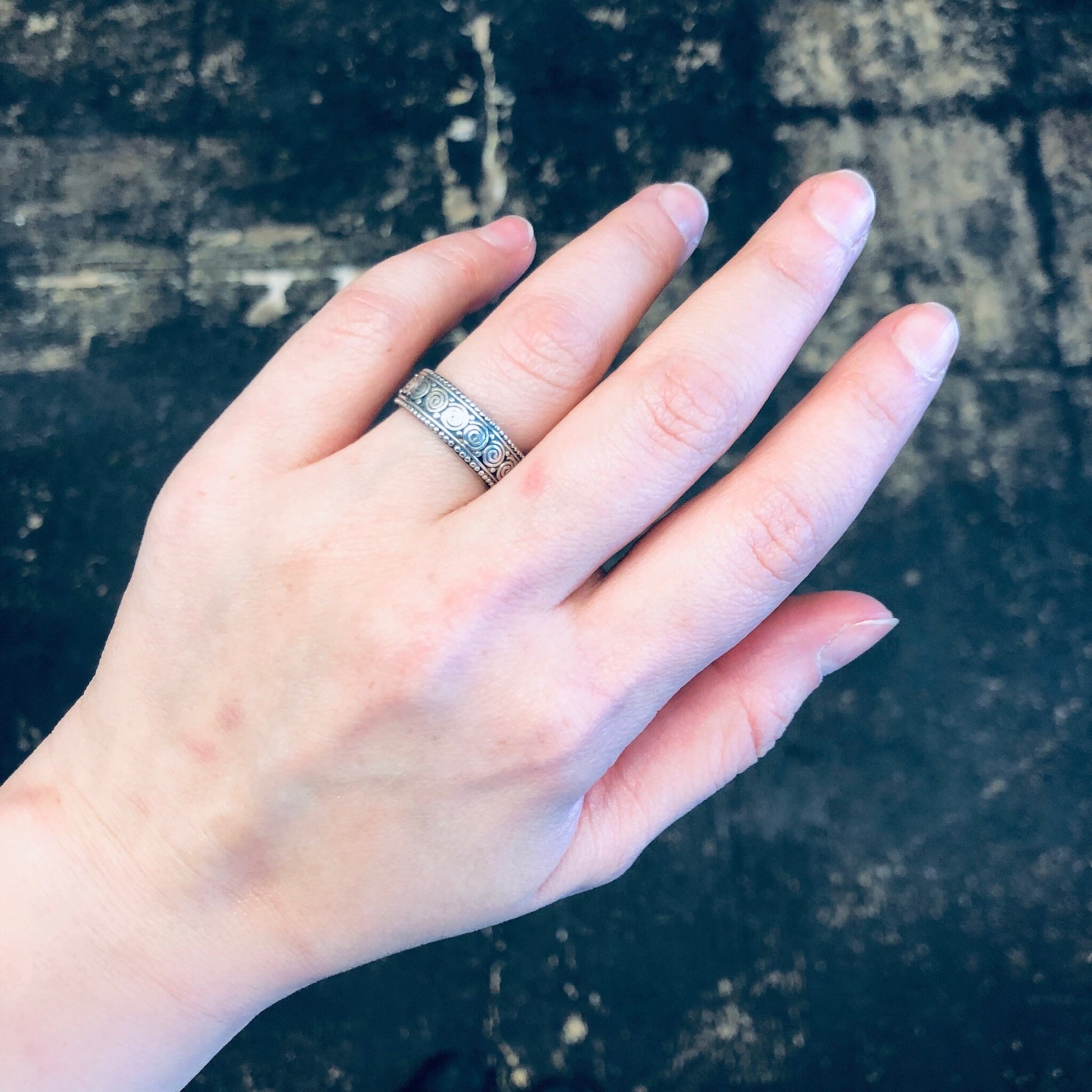 Vintage silver swirl design band ring on hand against textured dark background