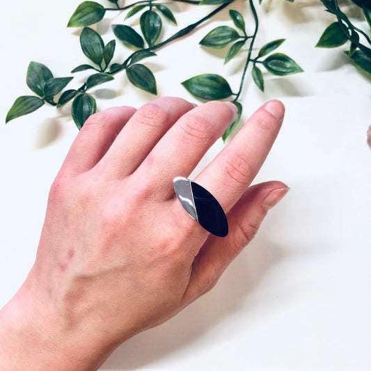 Hand modeling a vintage silver ring with black onyx, featuring an abstract minimalist design against a white background with green foliage.