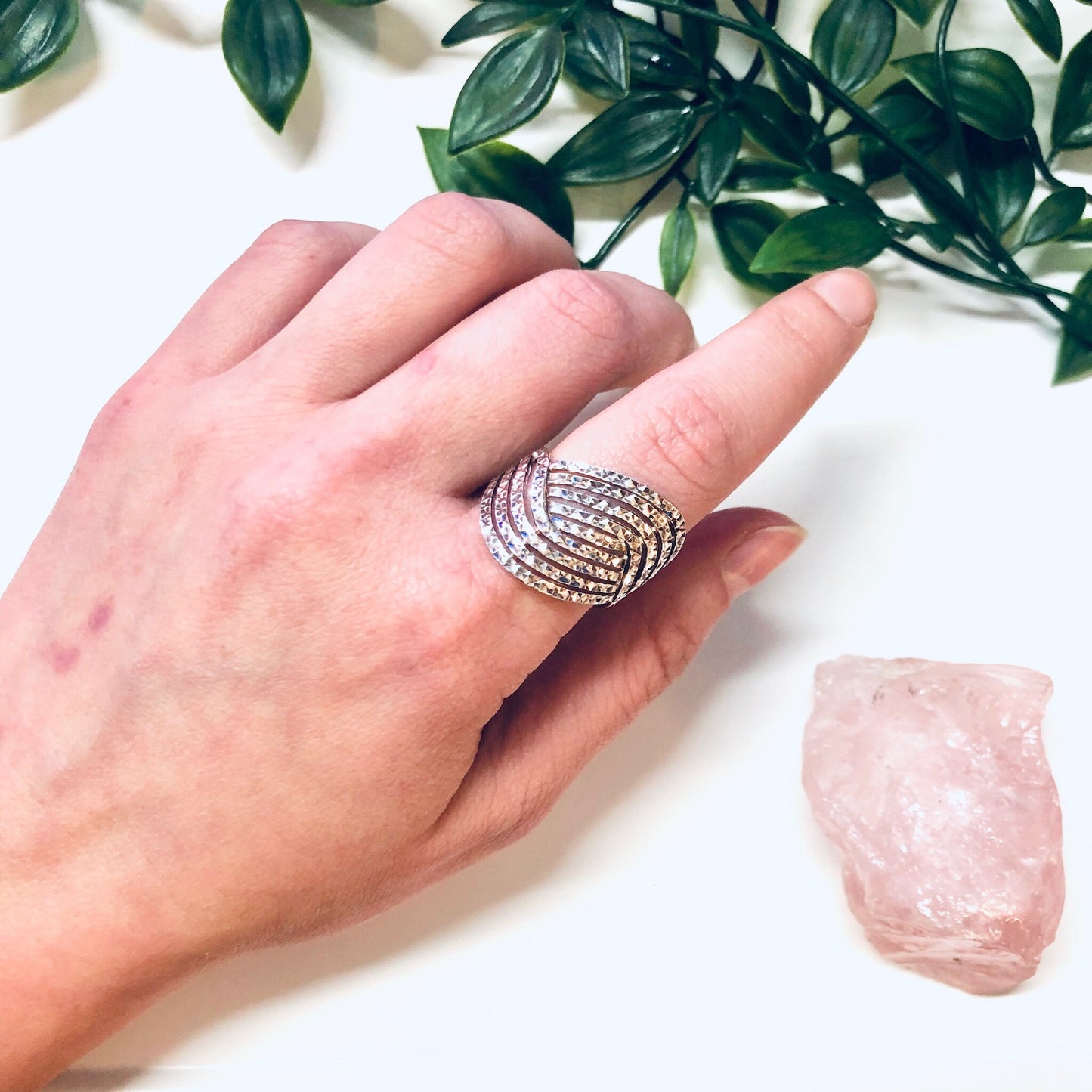 Vintage silver wave design ring with sparkly crystals on a hand, next to rose quartz crystal and green leaves