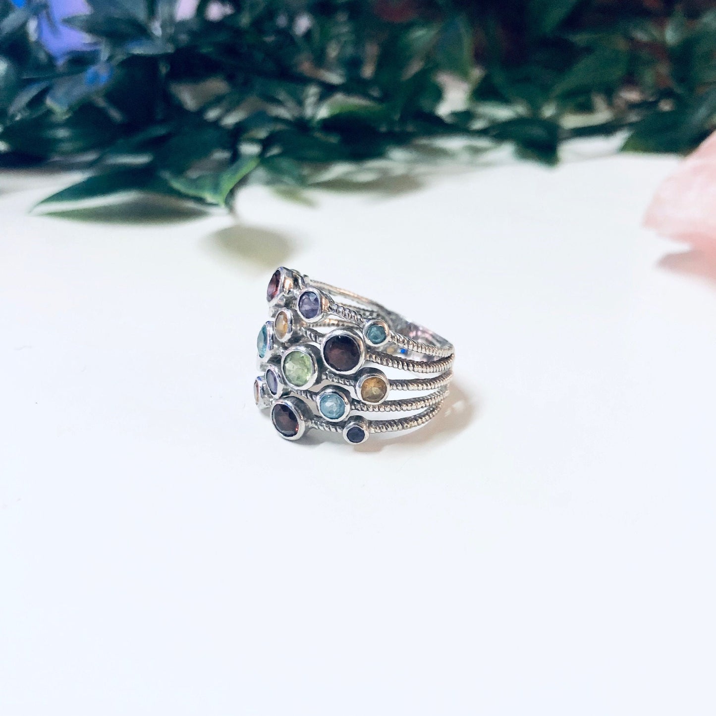 Vintage silver multi-band ring with colorful gemstones in purple, blue, red, green, and yellow hues, crafted from 925 silver. Large statement jewelry piece resting on white background with greenery.