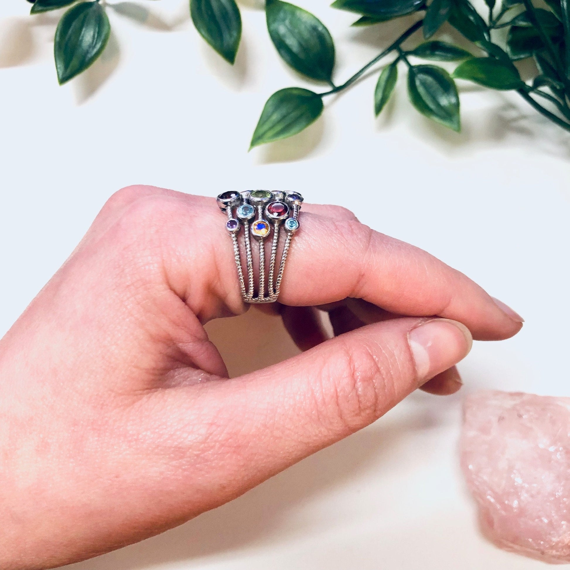 Vintage silver multi-band statement ring with colorful purple, blue, red, green and yellow gemstones, held in hand with leaves and rocks in background