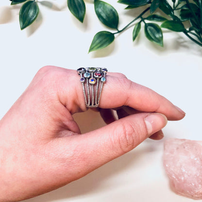 Vintage silver multi-band statement ring with colorful purple, blue, red, green and yellow gemstones, held in hand with leaves and rocks in background