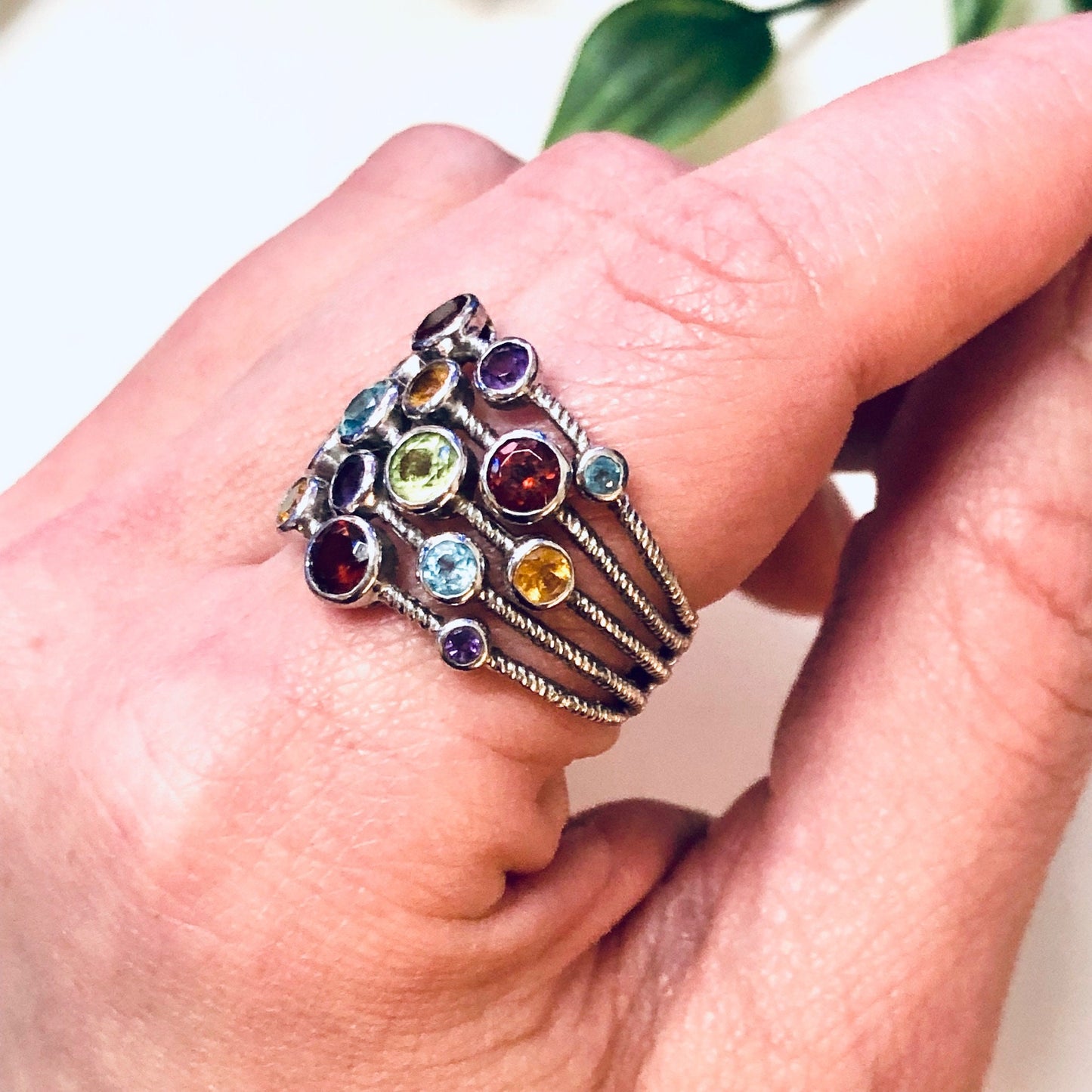 Vintage silver multi-band ring with colorful gemstones in purple, blue, red, green and yellow tones, worn on a finger. Statement jewelry piece with an eye-catching, bold design featuring multiple thin silver bands adorned with round faceted gems.