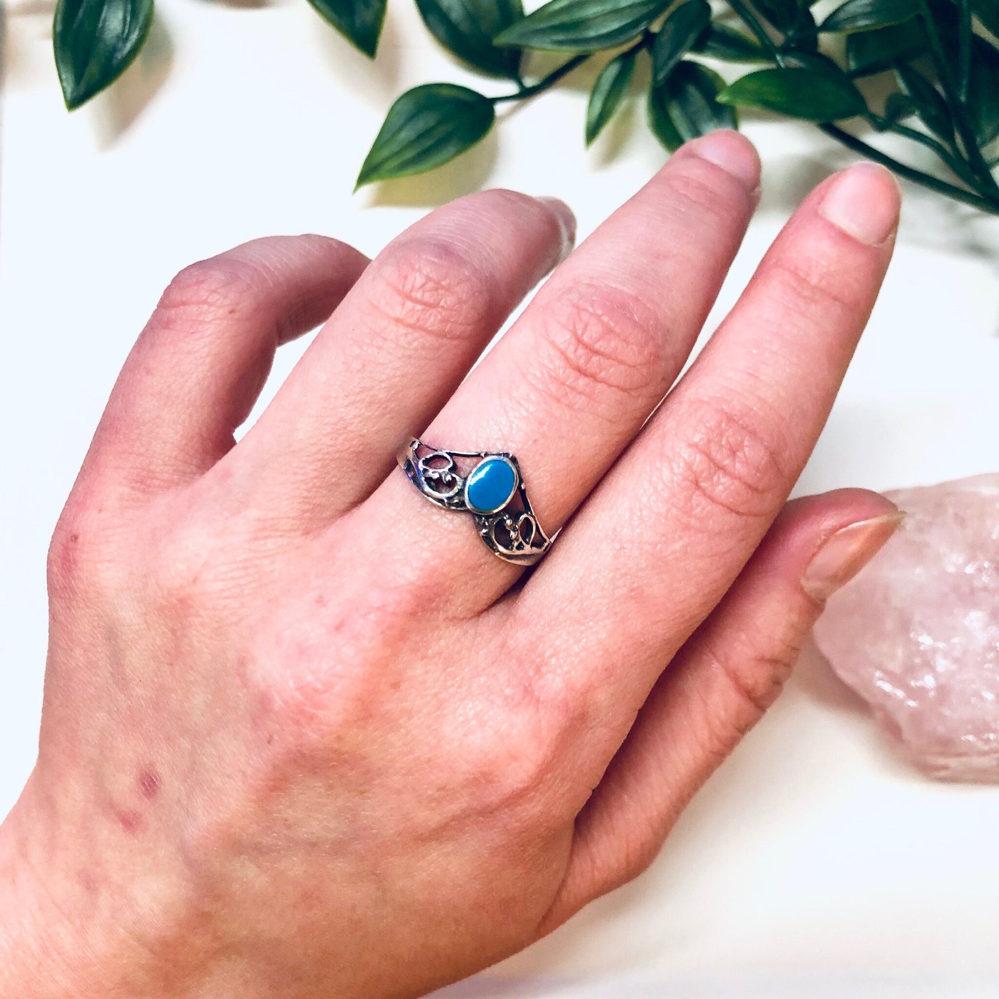 Vintage silver and turquoise V-shaped stacking ring on hand with greenery in background