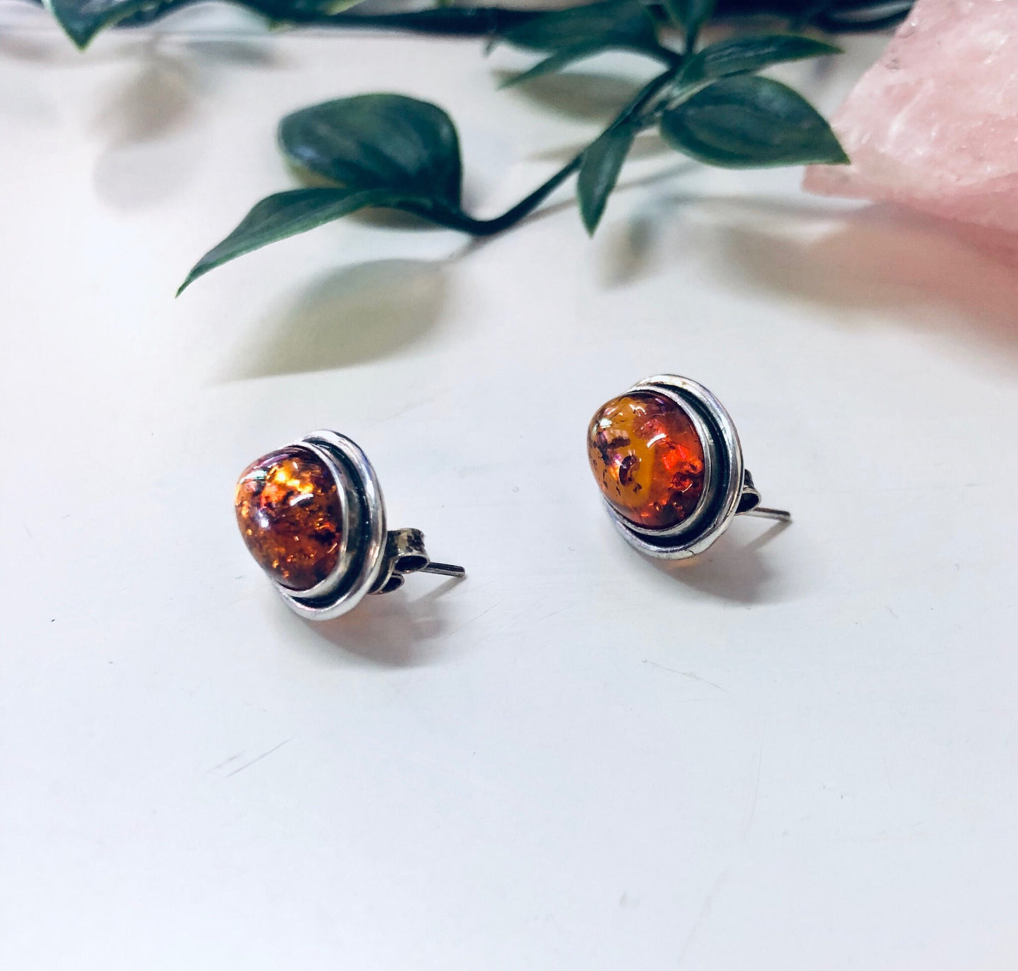 Vintage silver and amber stud earrings on white fabric with pink flowers and green leaves in soft focus background