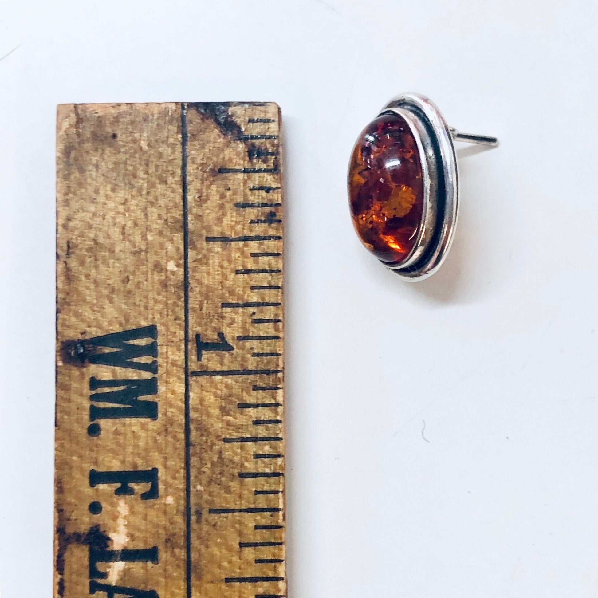 Vintage amber stud earrings in silver setting, showing ruler for scale against white background.