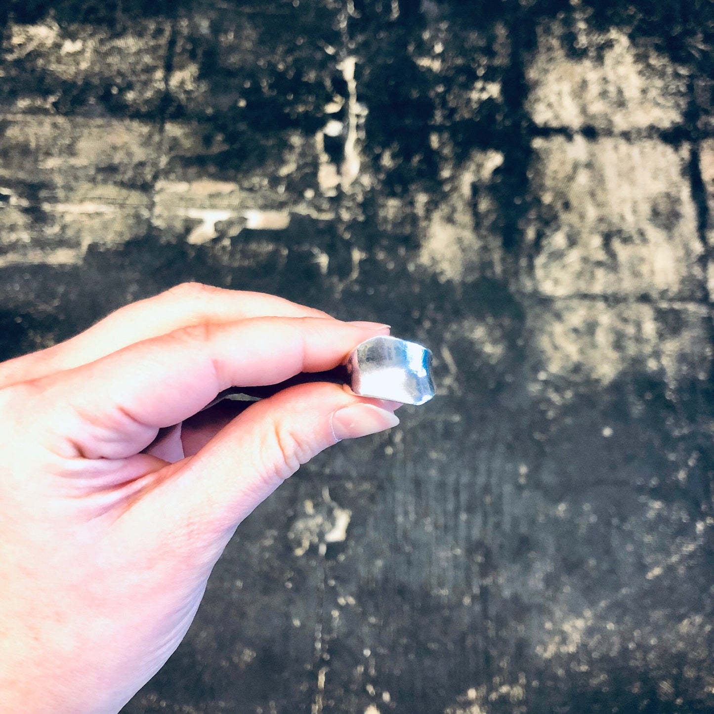 Hand holding a vintage silver band ring against a weathered concrete background