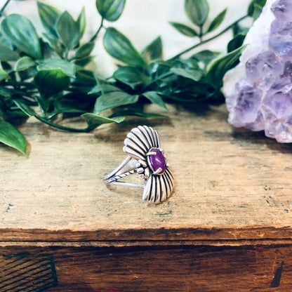 Vintage silver fan design ring with purple gemstone on rustic wooden surface with greenery in background, unique boho style statement jewelry.