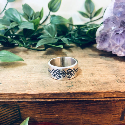 Vintage silver geometric tribal design band ring on wooden surface with foliage and amethyst crystal in background