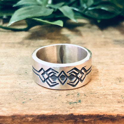 Vintage silver band ring with geometric tribal design pattern on rustic wooden surface with green foliage in background